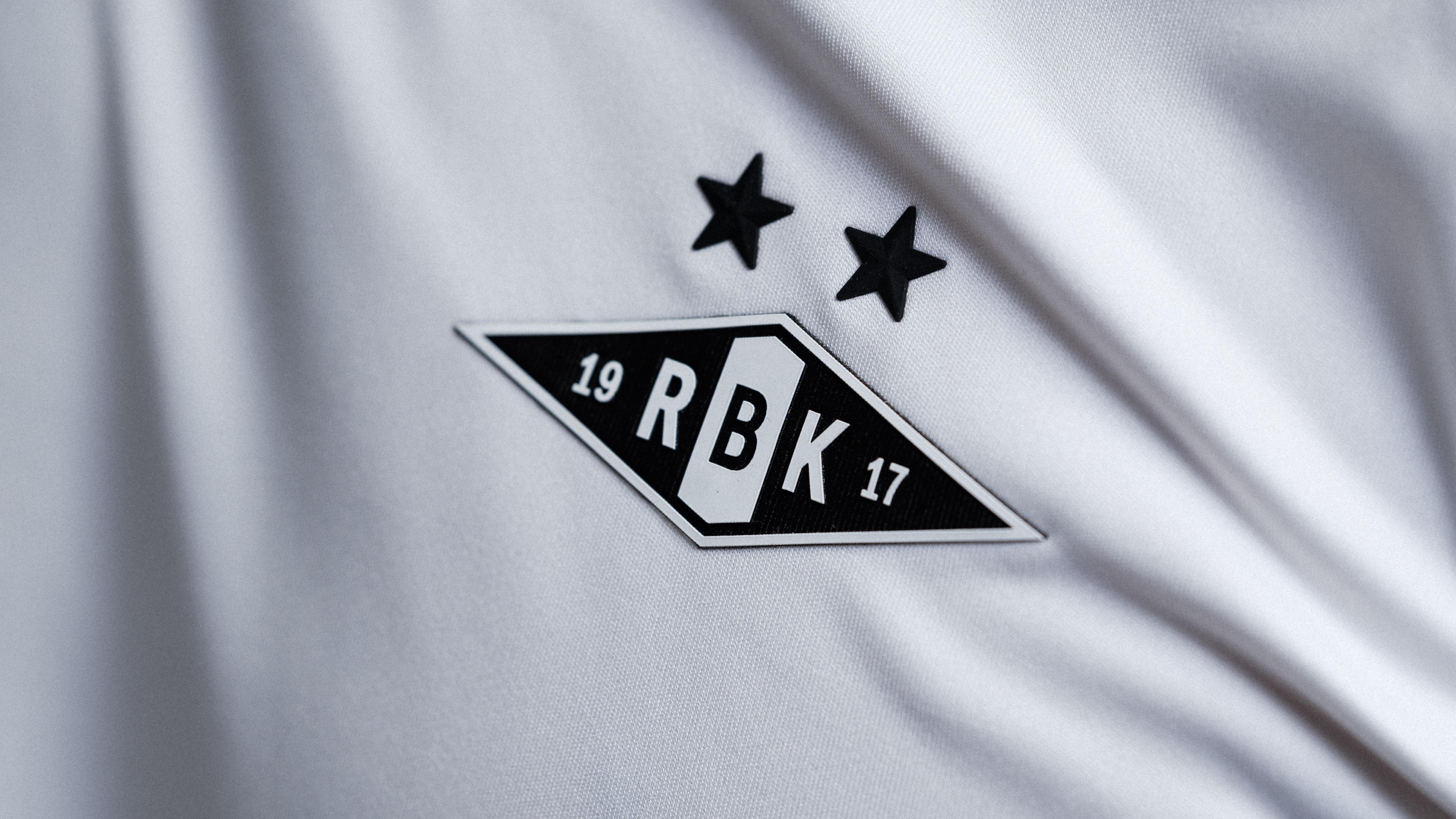 Nærbilde av Rosenborg BK-emblemet med to svarte stjerner brodert på en hvit fotballdrakt.