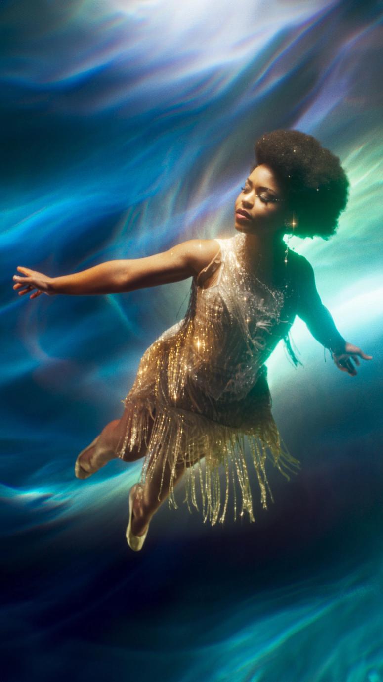 En danser med afro svever i luften iført en glitrende gullkjole med frynser mot en blå drømmende bakgrunn — av Nonspace
