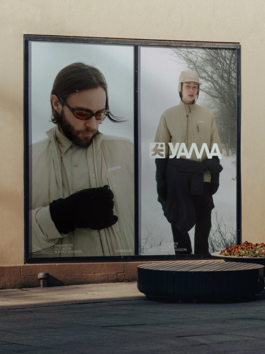 Reklameplakat for Yama med to modeller i beige utendørsjakker mot en vinterbakgrunn — av Nonspace