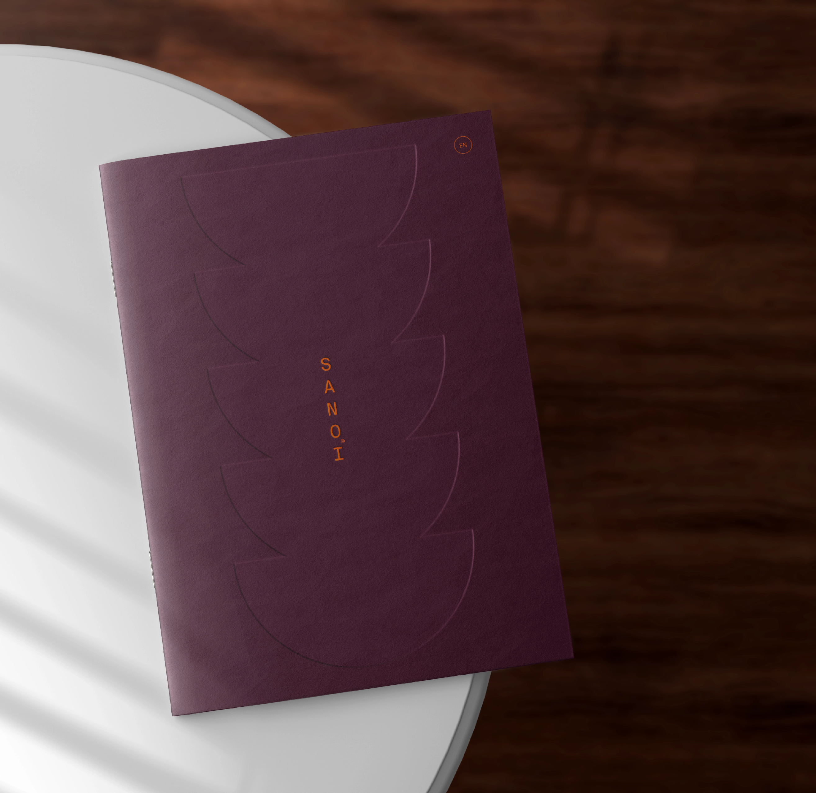 A purple menu or booklet with "SANOI" text and embossed curved shapes on a white table — by Nonspace
