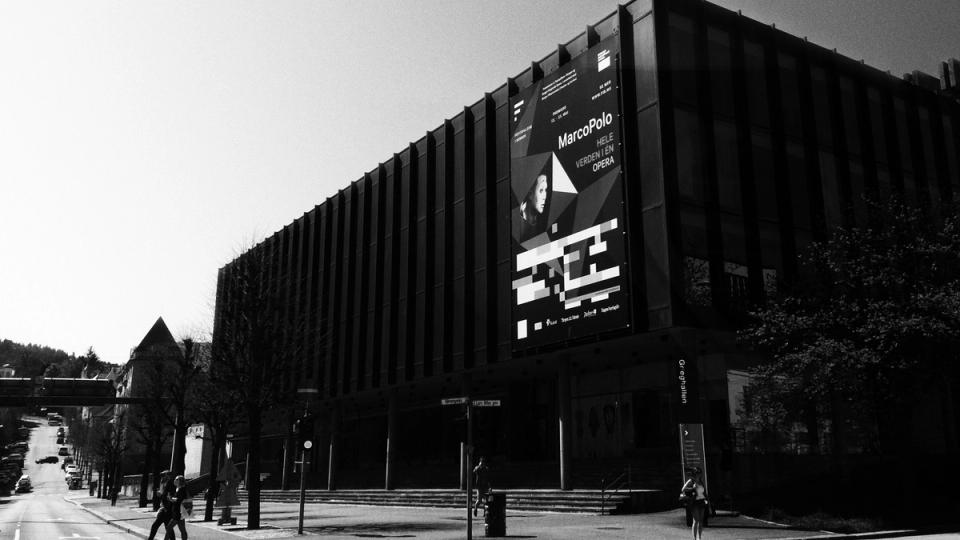 A modernist building facade displaying a large Marco Polo opera promotional banner with geometric design elements — by Nonspace