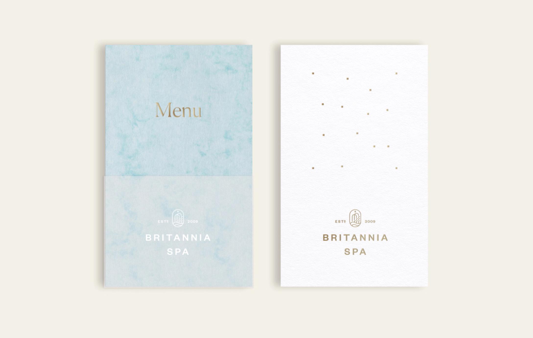 En lyseblå meny og et hvitt kort med gulldetaljer og logo for Britannia Spa etablert 2009 — av Nonspace