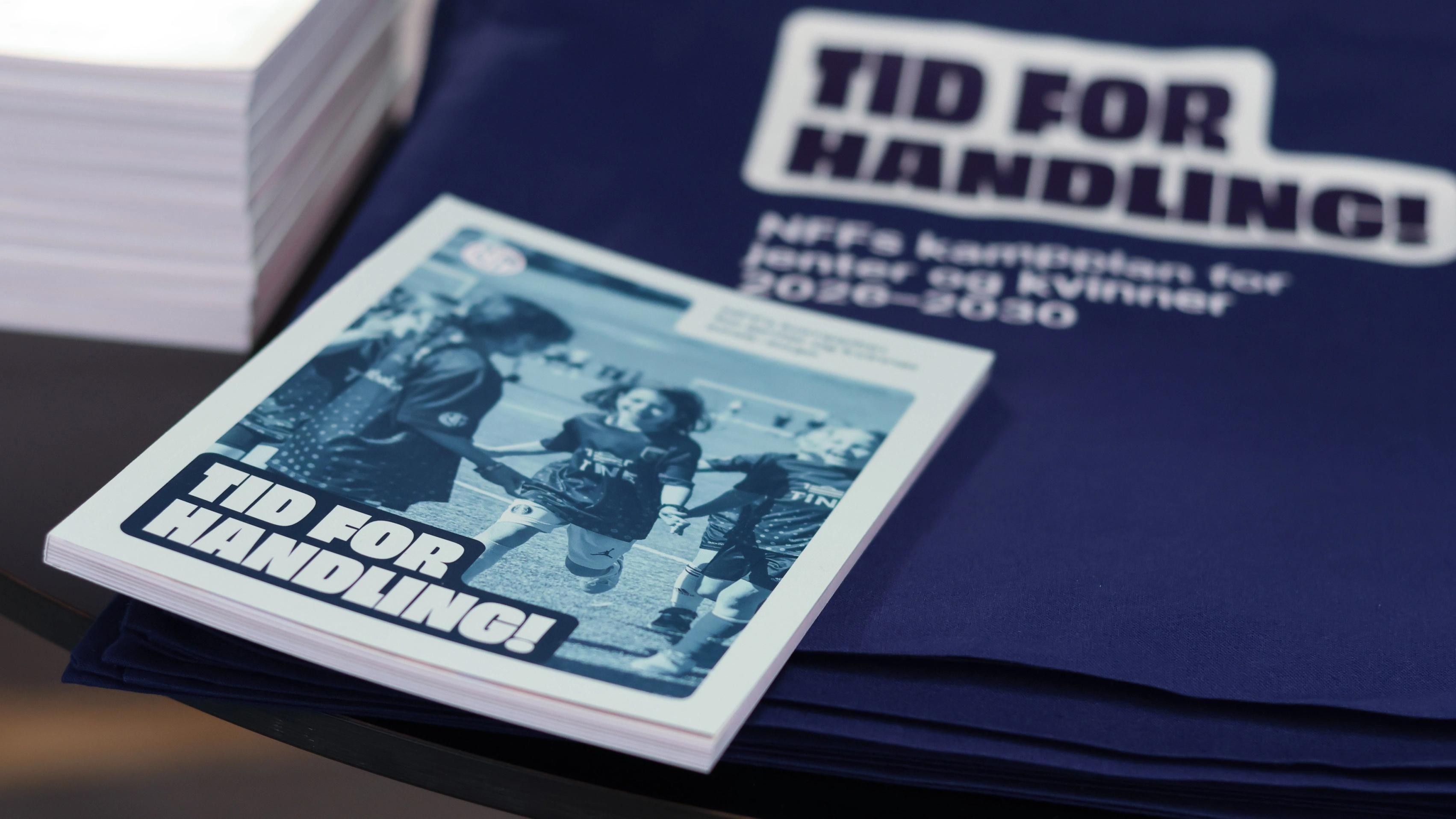 Printed strategy report with a Time for action cover resting on a dark blue tote bag carrying the campaign title and the subtitle NFF's match plan for girls and women 2026-2030.