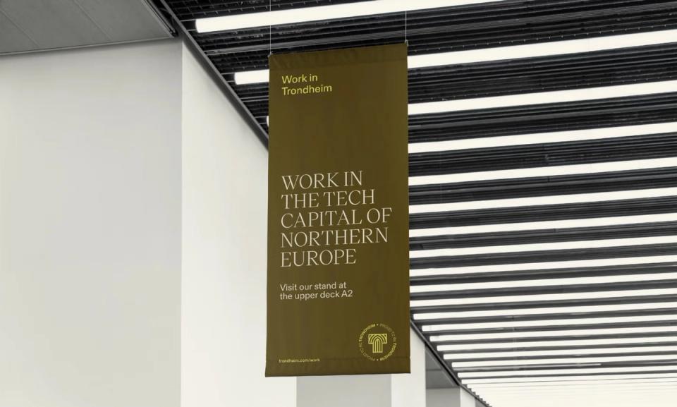 Et olivengrønt banner med teksten "Work in the Tech Capital of Northern Europe" henger fra taket i et moderne lokale — av Nonspace