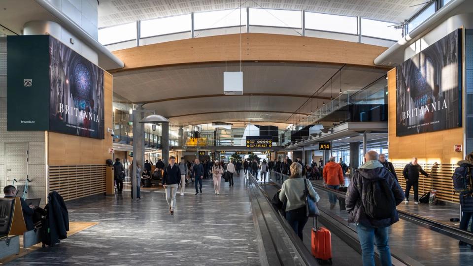 Airport terminal with travelers and moving walkways featuring large Britannia Hotel advertisements on both sides — by Nonspace