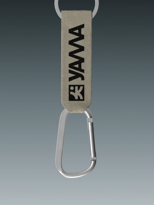 A tan woven keychain strap with black Yama logo attached to a silver carabiner and key ring — by Nonspace