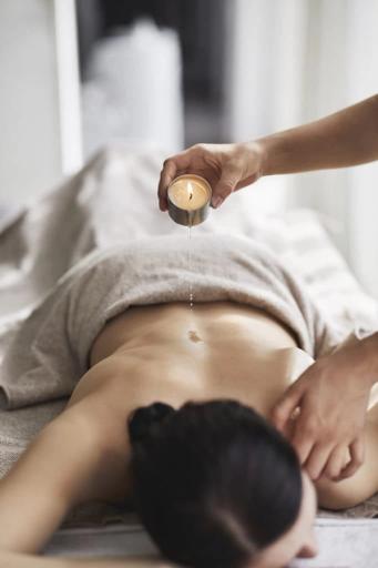 En person ligger på spa-benk mens varm olje helles fra et massasjestearinlys på magen — av Nonspace