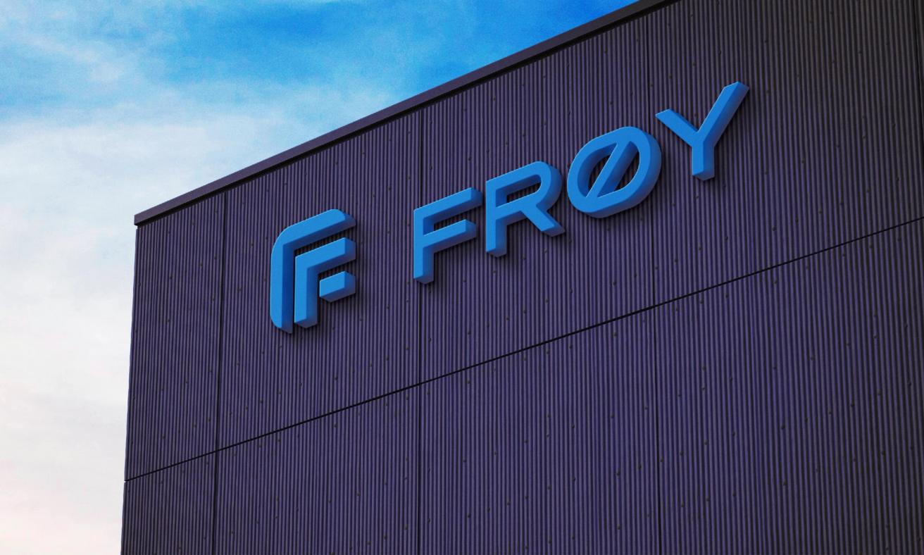 A blue 3D FRØY logo sign mounted on a dark corrugated metal building facade against a blue sky — by Nonspace