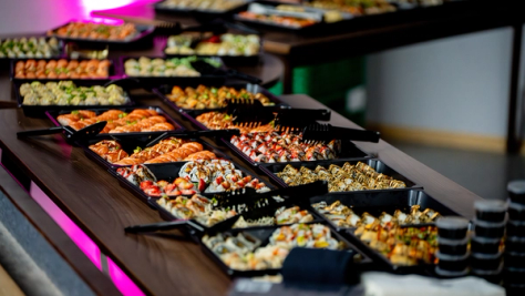 Et langbord med mange svarte fat fylt med variert sushi under rosa belysning — av Nonspace