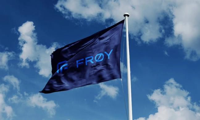 A dark blue flag with the Frøy logo flying against a cloudy sky — by Nonspace