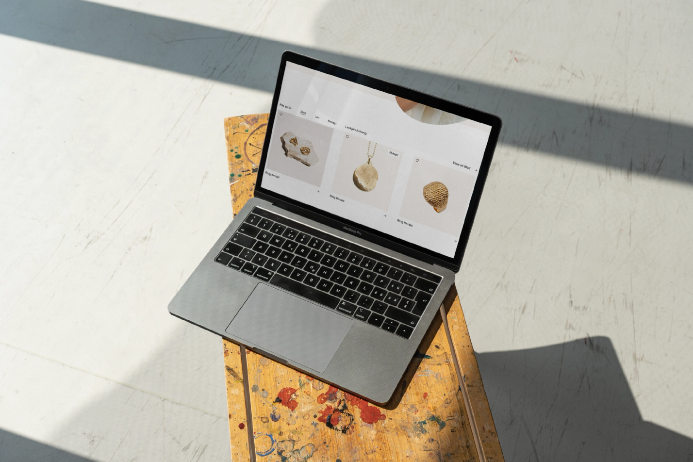 En MacBook Pro på et malt trebord viser en nettbutikk med gullsmykker i sollys — av Nonspace