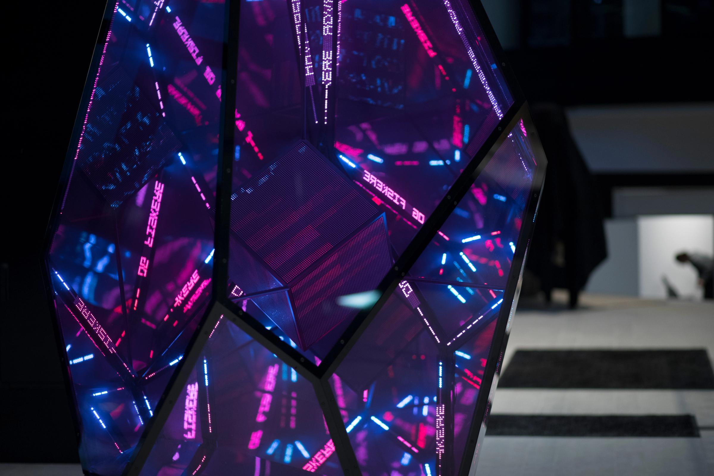 En geometrisk skulptur med LED-lys og speilende flater som viser uendelige refleksjoner i lilla og blått — av Nonspace
