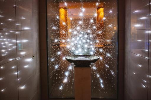 En dekorativ fontene med en skål på pidestall omgitt av lysende vanndråper i en elegant spa-setting — av Nonspace