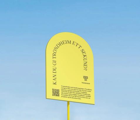 A yellow arched sign asking "Can you give Trondheim one second?" in Norwegian with a QR code and project details — by Nonspace