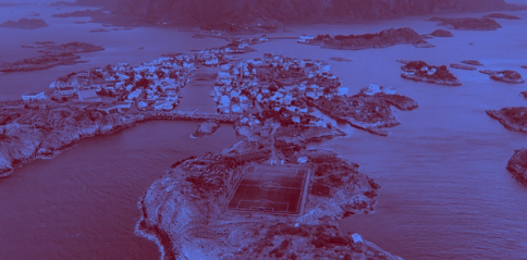 Aerial view of a Norwegian coastal village with a football pitch on a small rocky island — by Nonspace