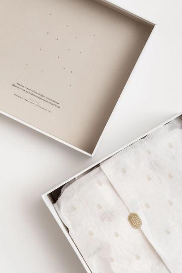 En elegant hvit gaveeske med beige innside og silkepapir med gullmønster som pakker inn et produkt — av Nonspace