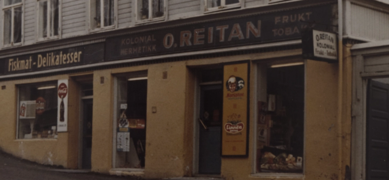 Et gammelt hjørnelokale med skiltet O. Reitan kolonial, hermetikk, frukt og tobakk fra midten av 1900-tallet — av Nonspace