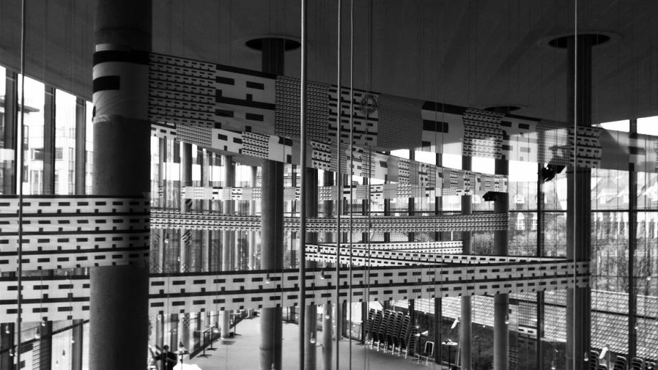 Interior view of a modern festival hall with geometric patterned glass walls and cylindrical columns — by Nonspace