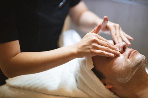 En kvinne får ansiktsbehandling med krem på en spa mens terapeuten masserer pannen hennes — av Nonspace