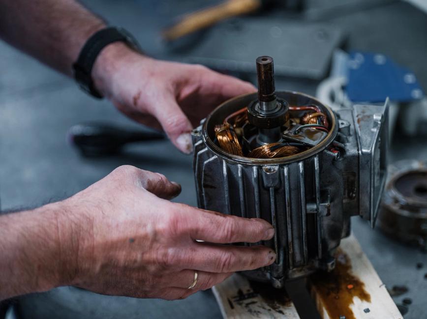 Et par hender arbeider med en elektrisk motor med synlige kobbervikling på et verksted — av Nonspace