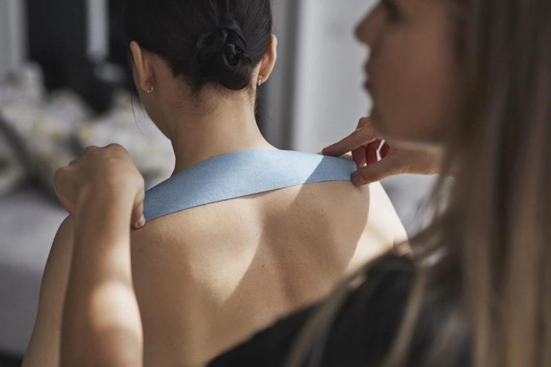 En terapeut applicerer kinesiotape på skuldrene til en kvinne med håret i en knute — av Nonspace
