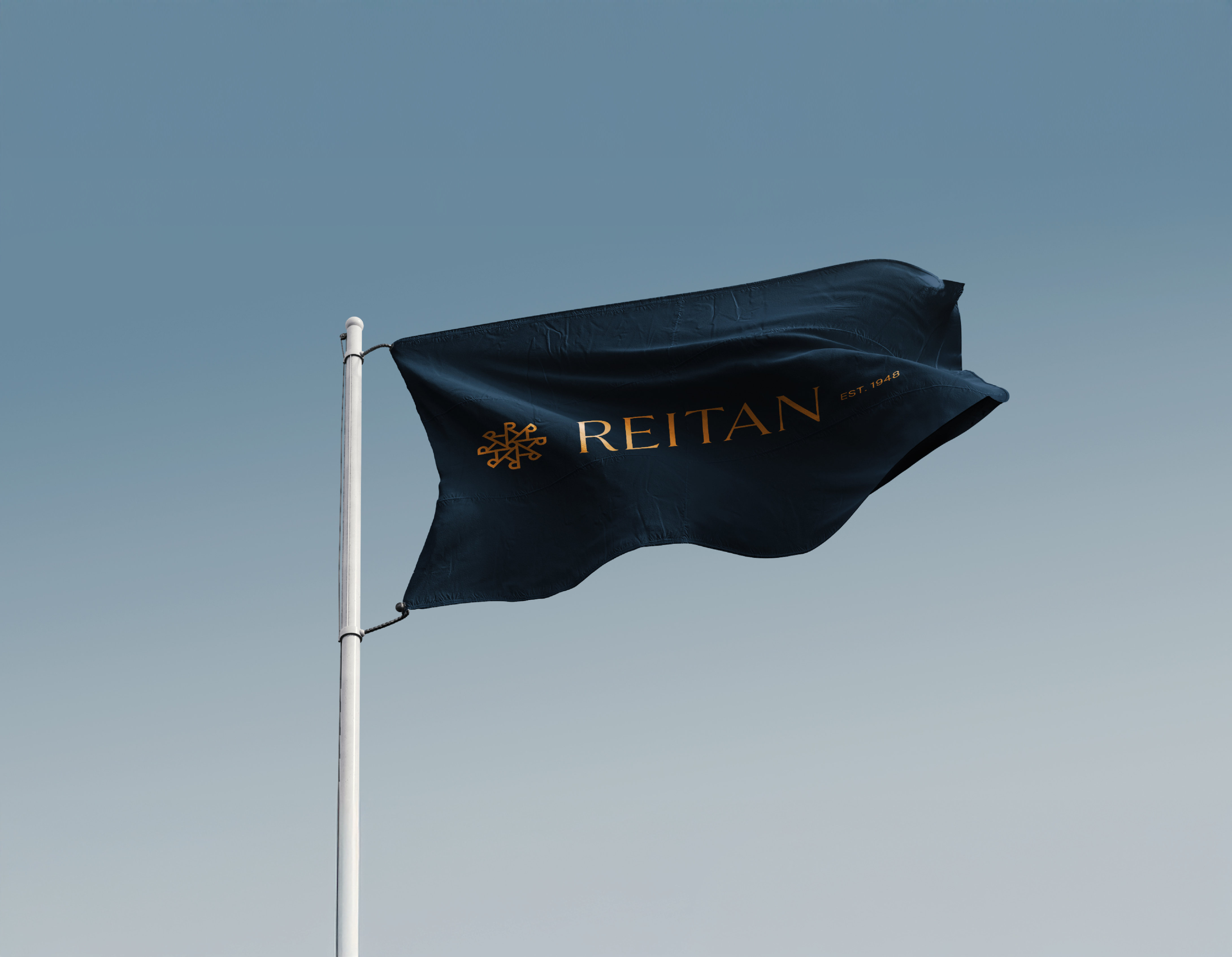 Et mørkeblått flagg med gullfarget Reitan-logo og "EST. 1948" vaier mot en klar blå himmel — av Nonspace