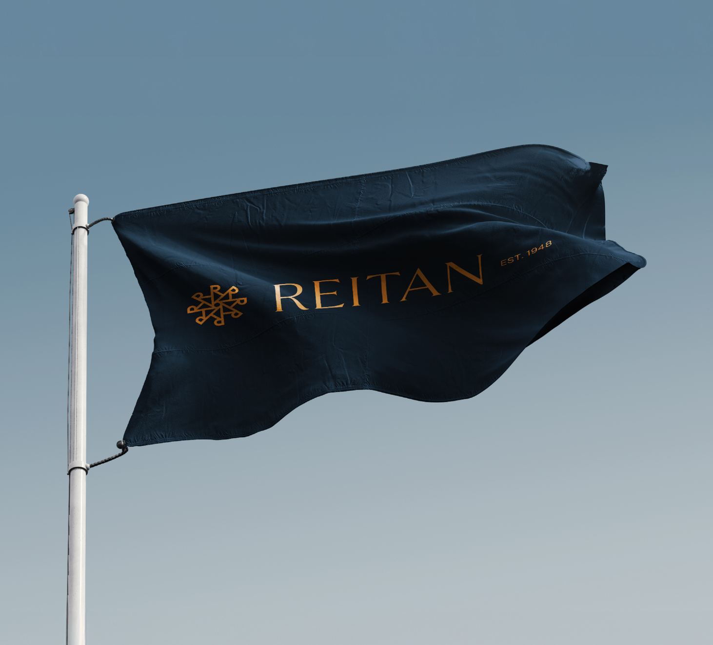 Et mørkeblått flagg med gullfarget Reitan-logo og "EST. 1948" vaier mot en klar blå himmel — av Nonspace
