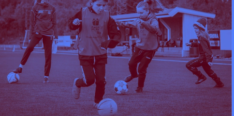 Barn i treningsklær spiller fotball på en kunstgressbane med flere baller under en økt — av Nonspace