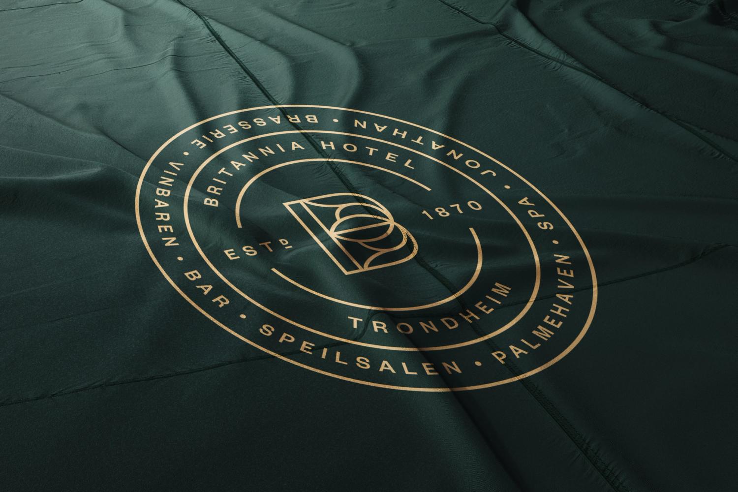 Gullfarget sirkulært emblem for Britannia Hotel Trondheim med logo og fasiliteter på grønn tekstil — av Nonspace