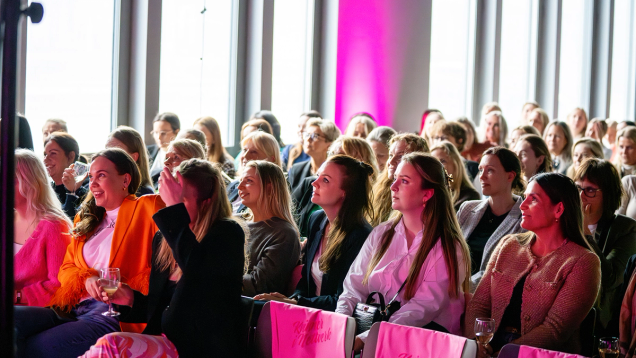 Engasjert publikum av kvinner sitter i rosa stoler og følger med på en presentasjon i et moderne lokale — av Nonspace