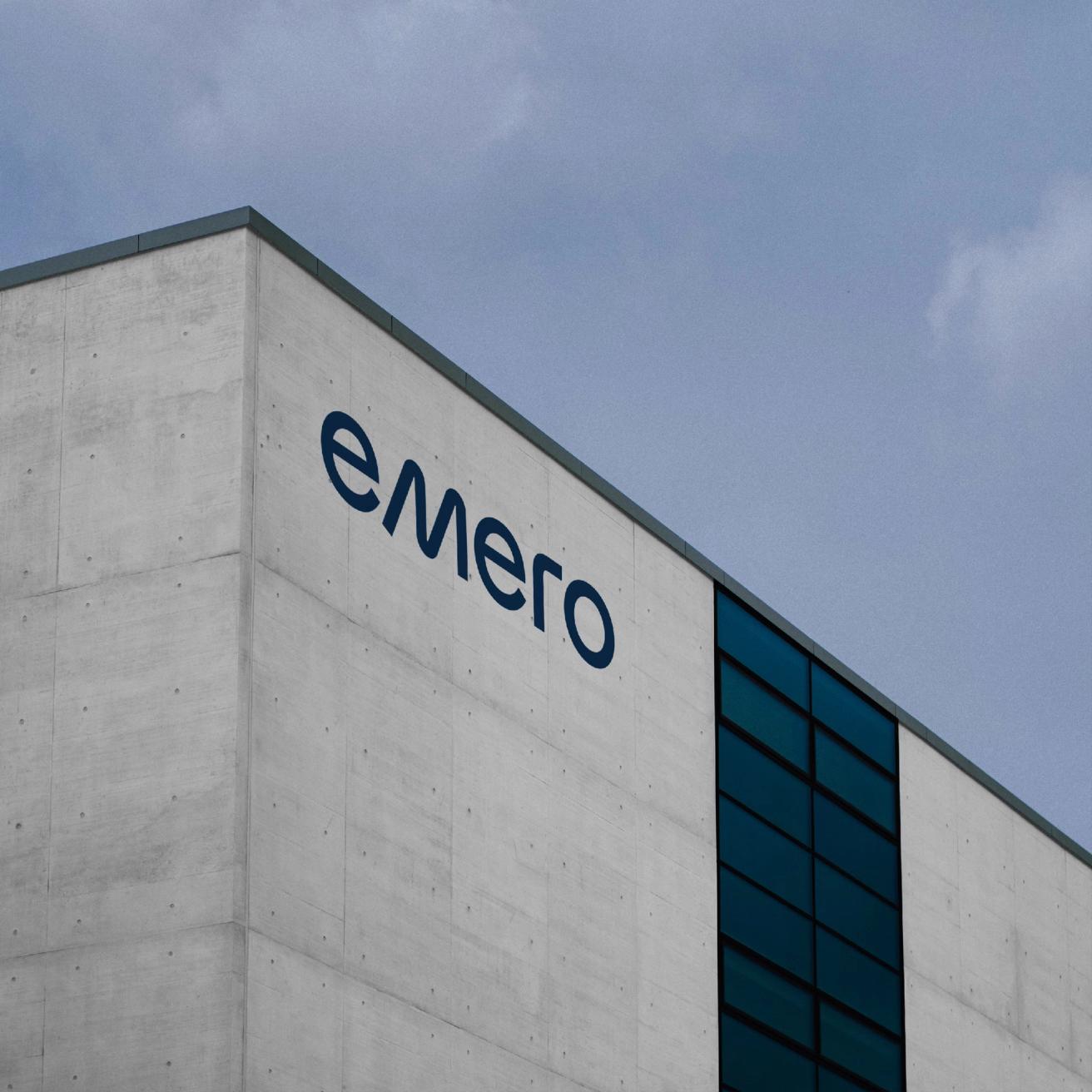 En moderne betongbygning med emero-logoen på fasaden og blågrønne vinduer mot en overskyet himmel — av Nonspace