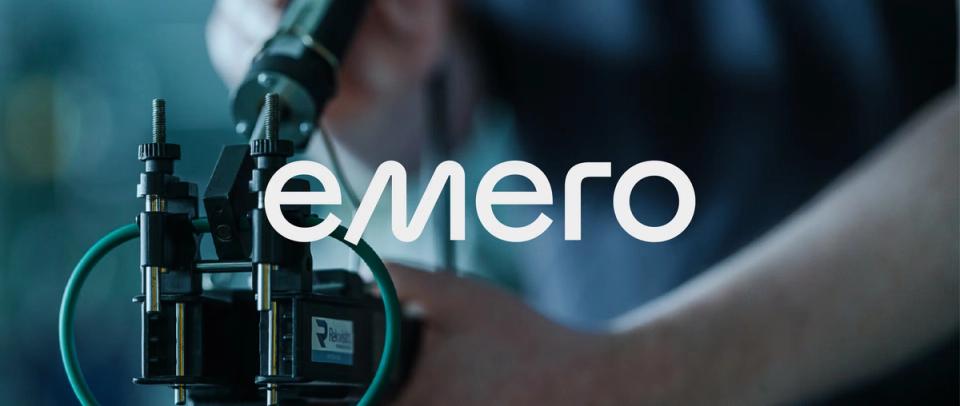En tekniker arbeider med industrielt utstyr med emero-logoen synlig i forgrunnen — av Nonspace