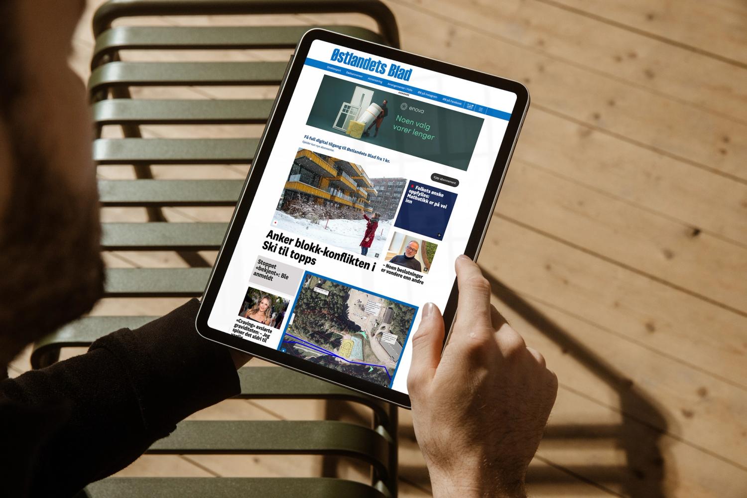 En person holder et nettbrett som viser forsiden til Østlandets Blad med en Enova-annonse øverst — av Nonspace