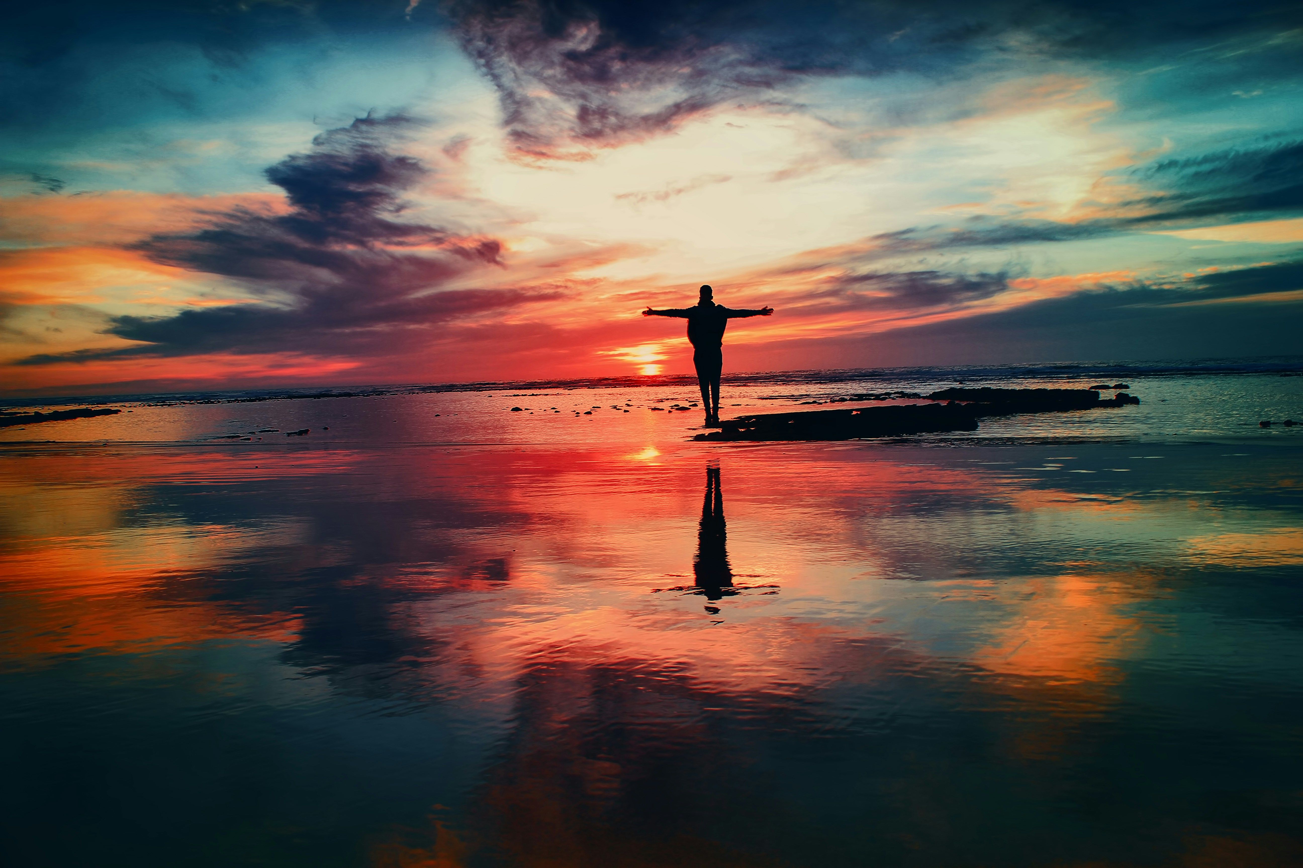 Person standing on a beach at sunset with arms open, symbolizing a fresh start after expungement in New Jersey