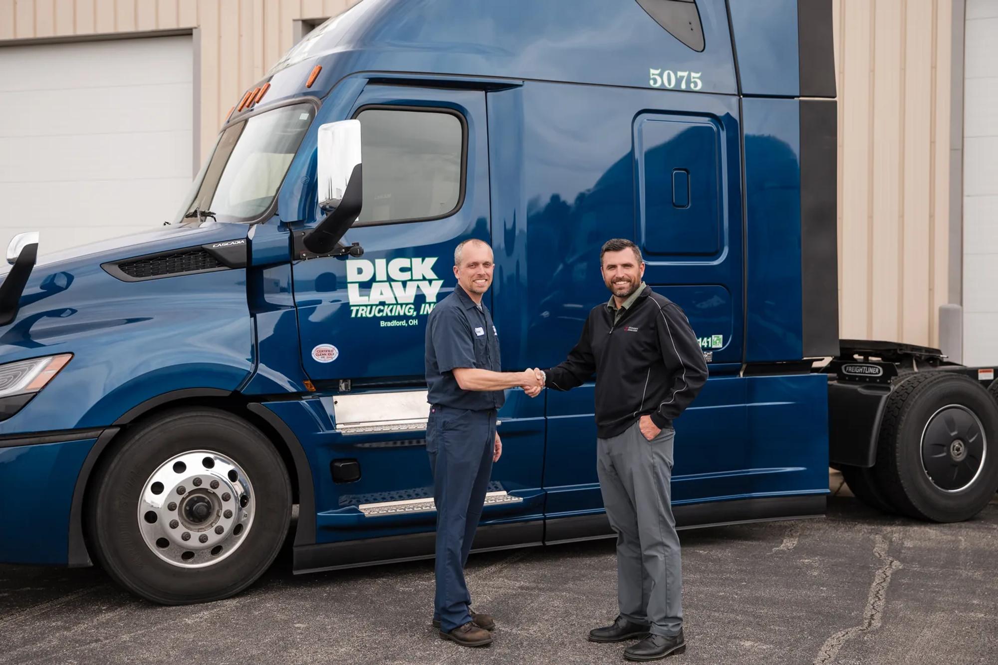Two men shaking hands in front of a branded Dick Lavy Freightliner dry van tractor