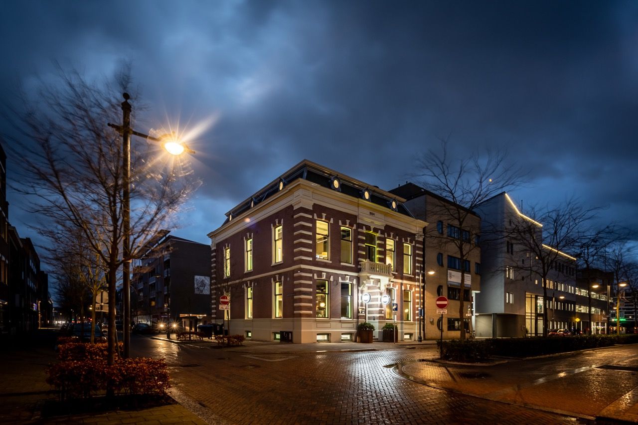Historic office building of An Apple A Day in Breda at dusk, located on a corner near the central station, with illuminated windows revealing the atmosphere inside the agency.