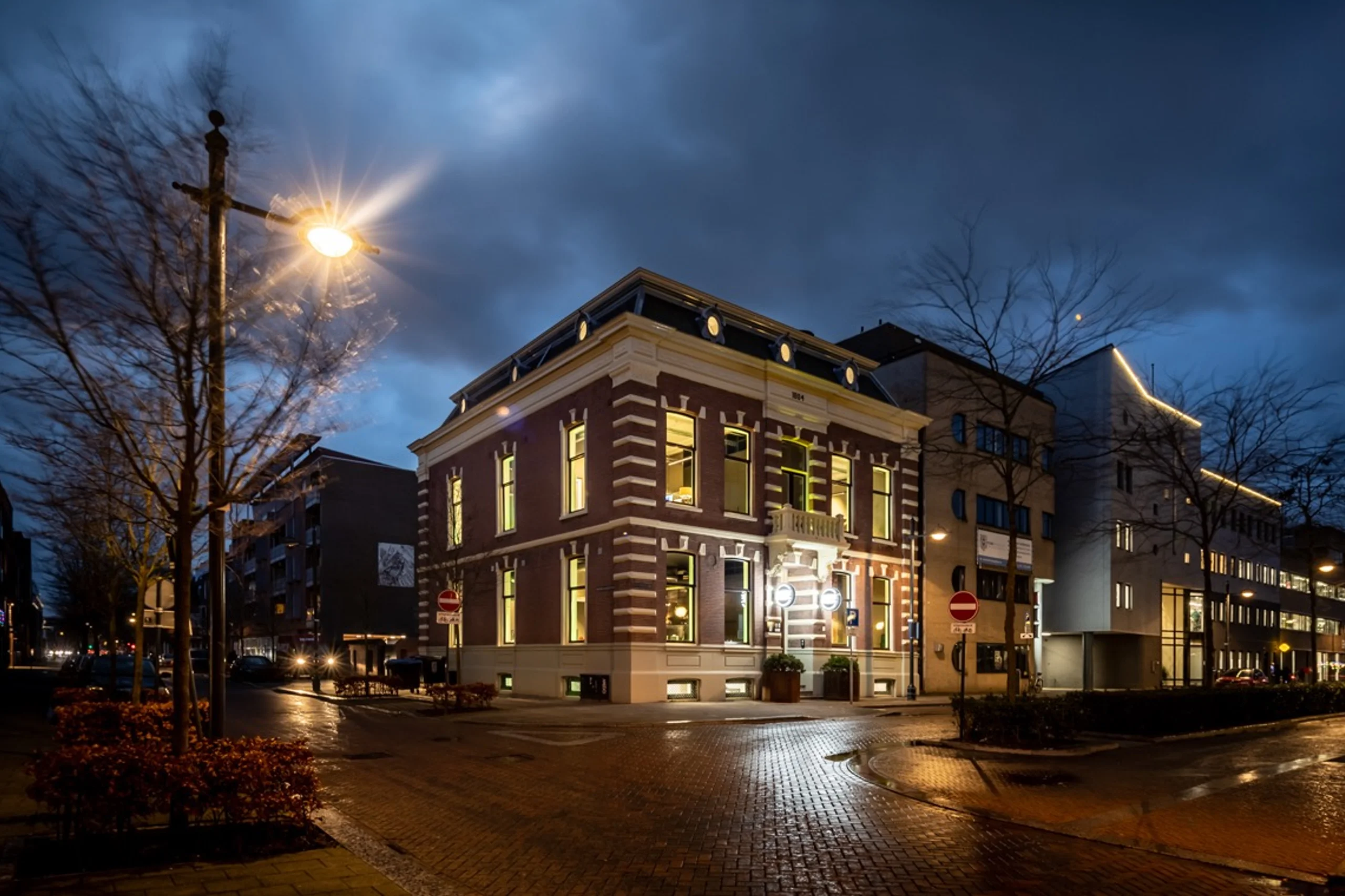 Historic office building of An Apple A Day in Breda at dusk, located on a corner near the central station, with illuminated windows revealing the atmosphere inside the agency.