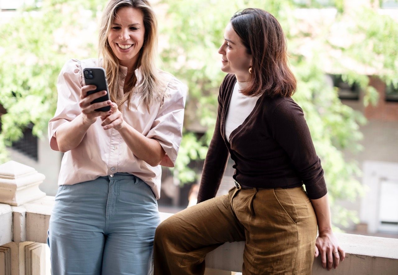 A red apple on a wooden table in the foreground, with a blurred view of four An Apple A Day colleagues in conversation during a team meeting in the background.