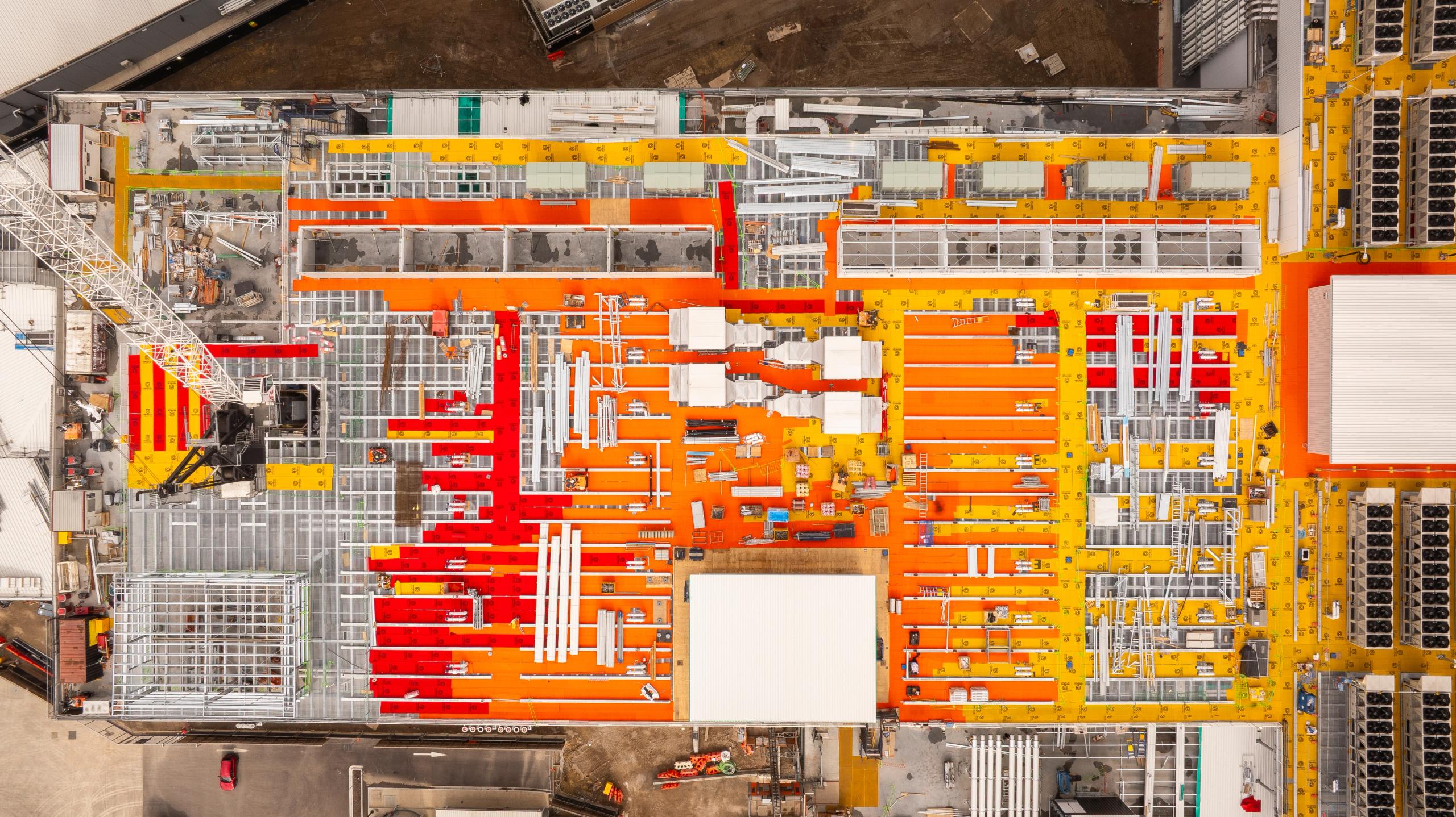 Aerial top-down view of dense rooftop mechanical and electrical services with orange and yellow pipework