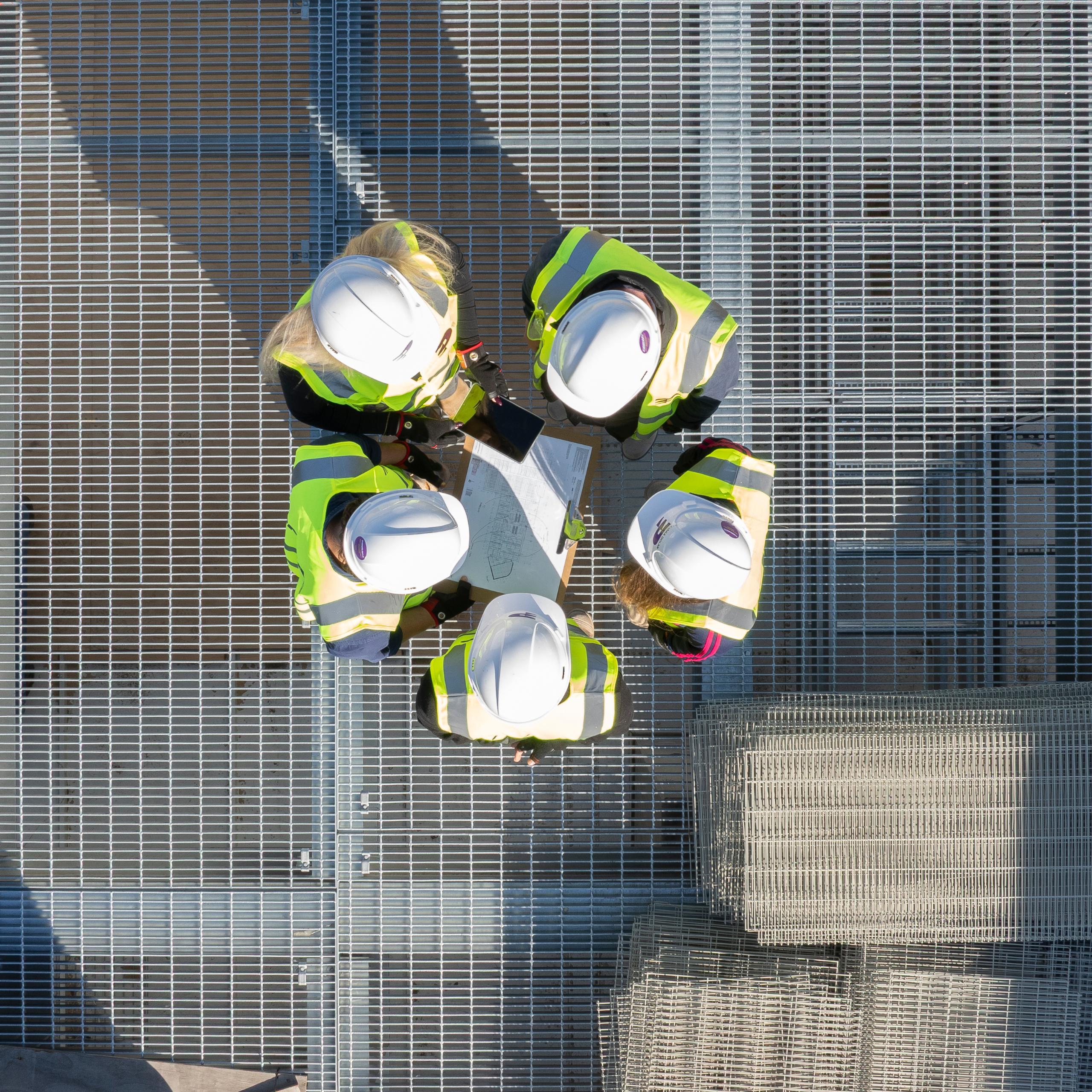 Aerial top-down view of construction workers in hard hats gathered in a circle on site