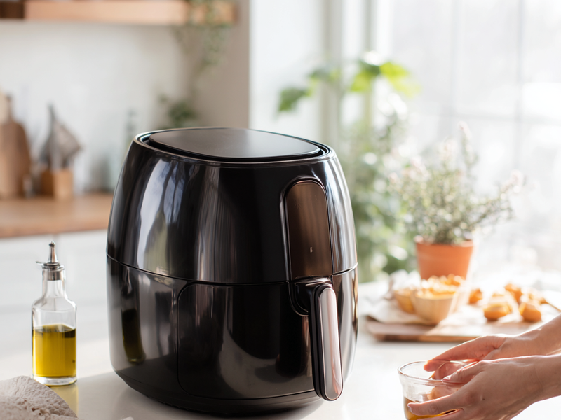Spraying air fryer basket with oil before cooking chicken parmesan
