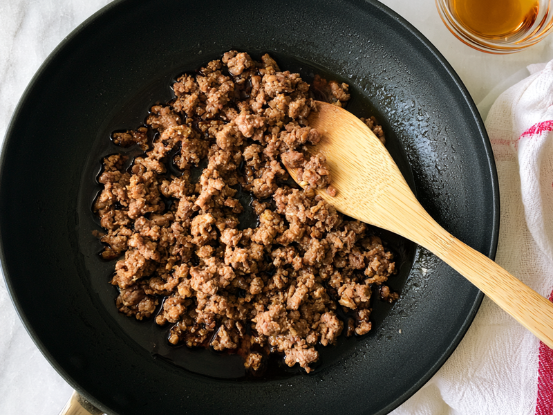 Ground beef browning in a skillet and being broken into small pieces.
