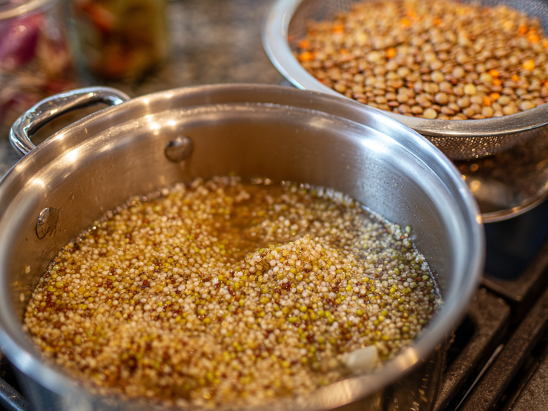 Quinoa simmering on the stove with lentils being rinsed and drained for bowl prep