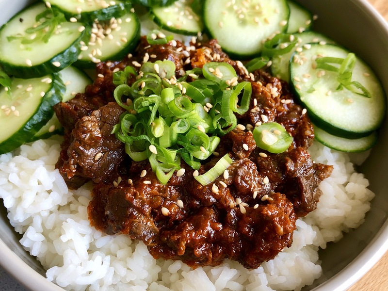 Rice bowls topped with spicy gochujang beef and sesame cucumber salad.