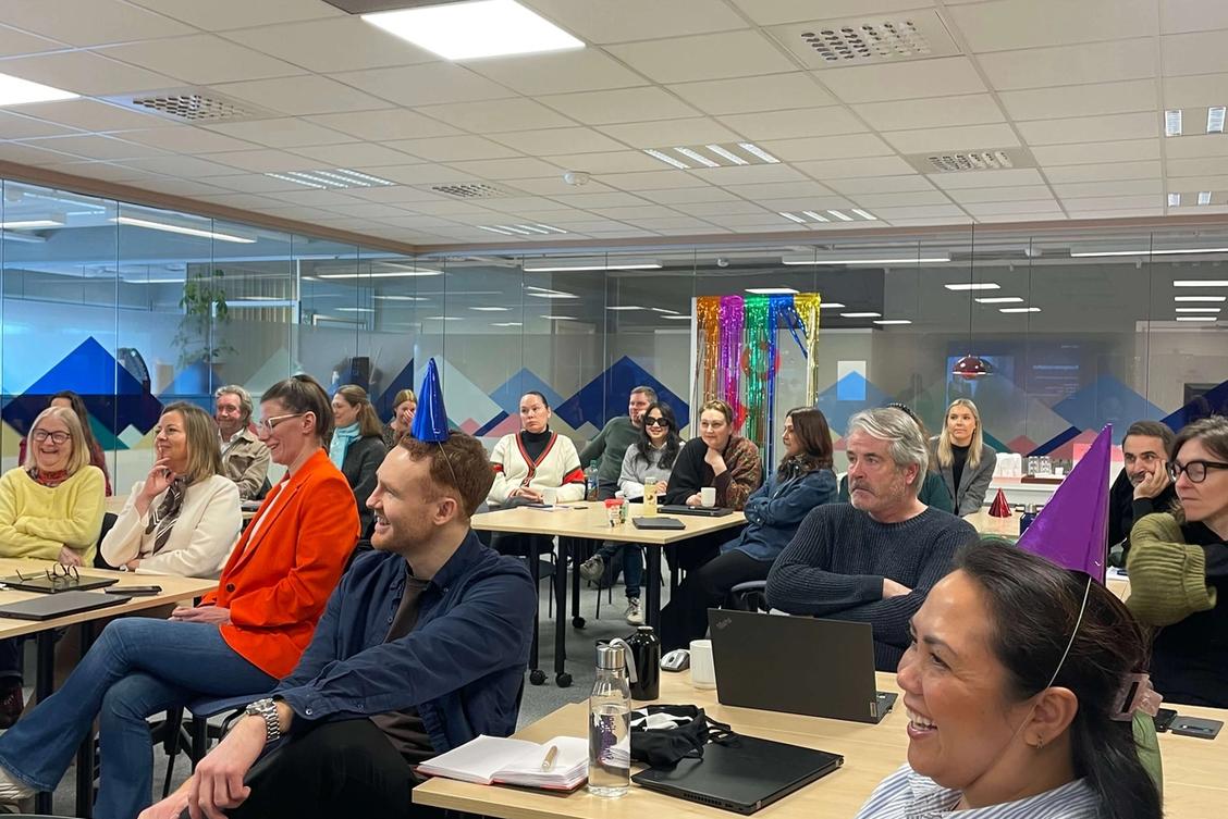 Bilde av en gruppe mennesker bak pulter. Noen har partyhatter på hodet.