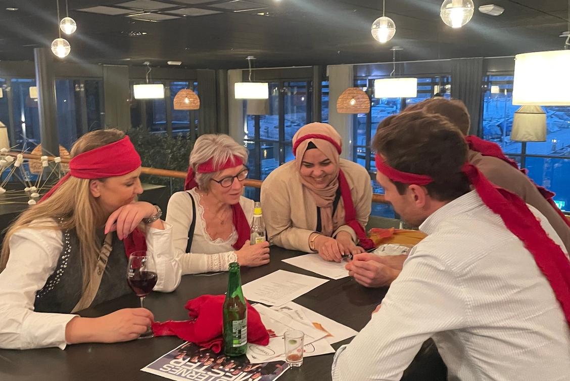 Bilde av en gruppe mennesker rundt et bord med røde sjerf på hodet.