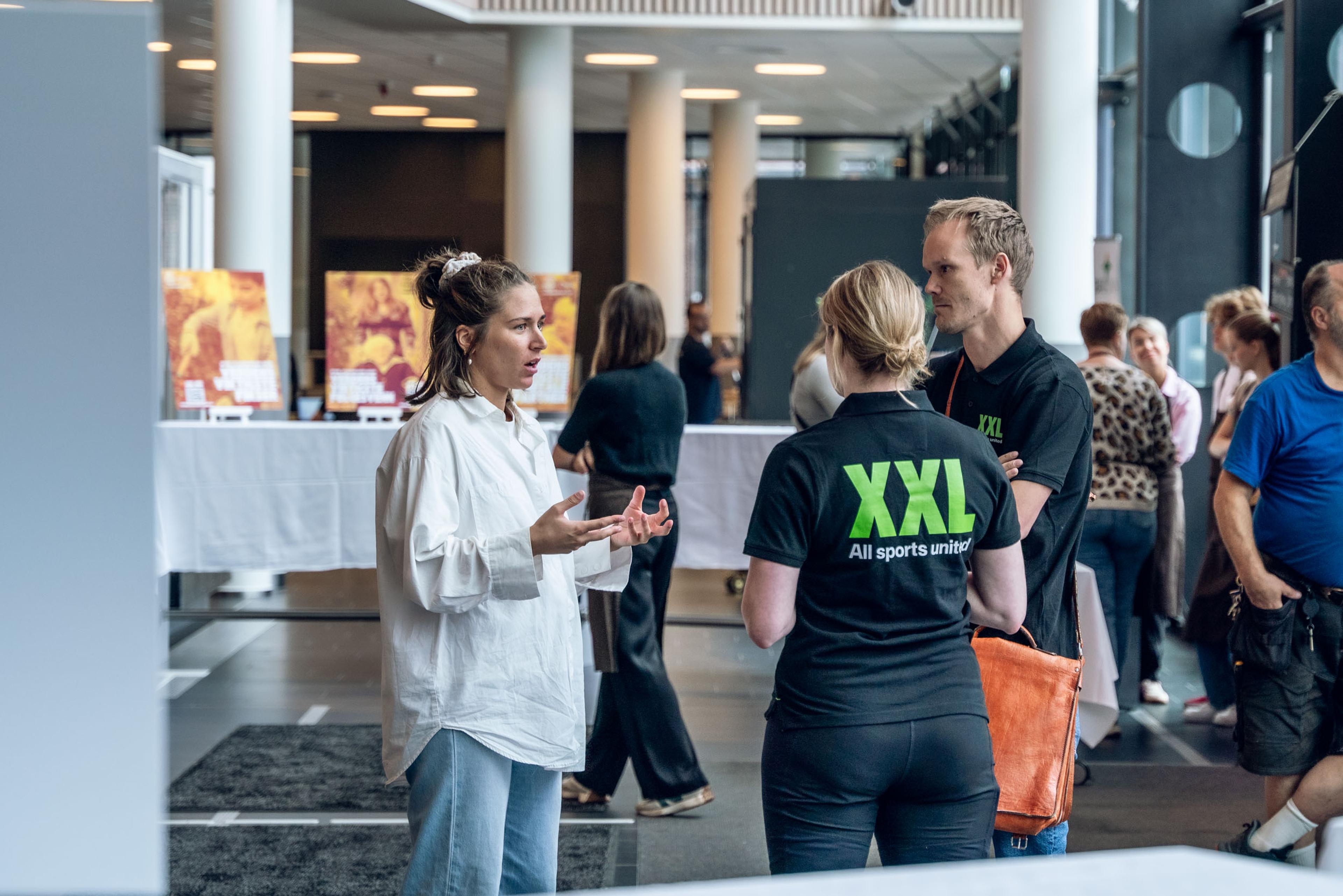 Bilde av tre personer i samtale. To av personene har XXL-t-skjorte på seg.