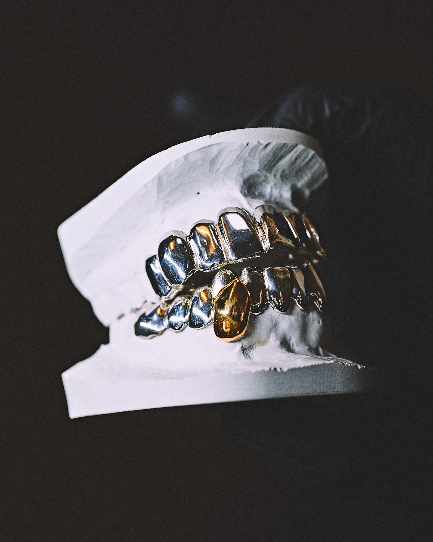 Grillz argent et or posé sur son modèle en plâtre, à l'atelier