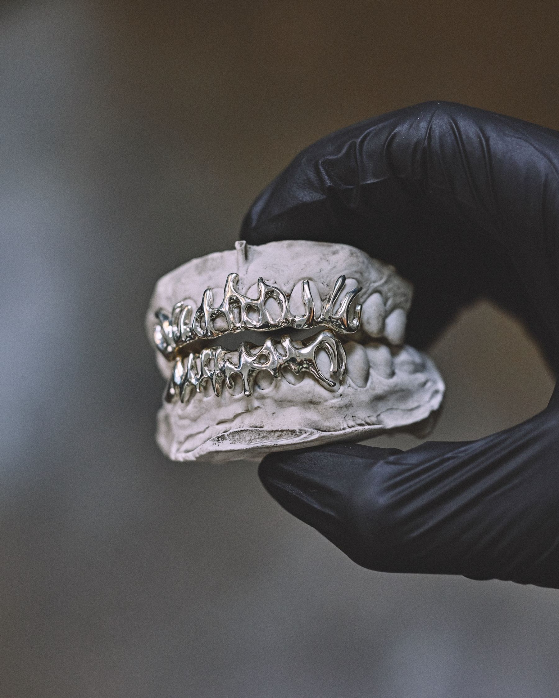 Main gantée tenant un grillz en argent au-dessus d'un moulage dentaire