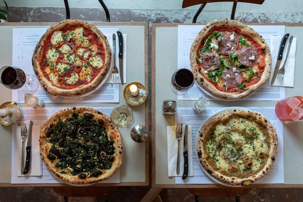 Vier Sauerteigpizzen von Gazzo von oben auf zwei Tischen, daneben Rotwein
